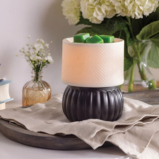 Lampe chauffe-cire électrique Luxe allumée, diffusant une lueur douce sur un meuble, créant une ambiance cosy sans flamme.