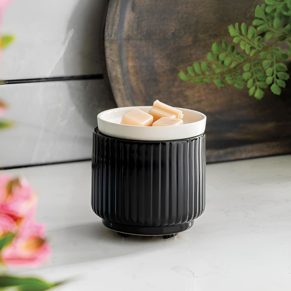 Gros plan de la Lampe à parfum avec plaque chauffante noir/blanc chauffant des cubes de cire beige sur un plan de travail en marbre, avec des fleurs roses en arrière-plan