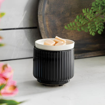 Gros plan de la Lampe à parfum avec plaque chauffante noir/blanc chauffant des cubes de cire beige sur un plan de travail en marbre, avec des fleurs roses en arrière-plan