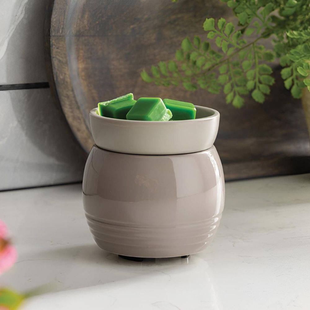La Lampe parfumée avec plaque chauffante ORB gris contenant des fondants de cire verte, posée sur un plan de travail en marbre devant un plateau en bois décoratif.