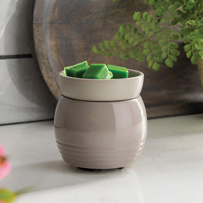 La Lampe parfumée avec plaque chauffante ORB gris contenant des fondants de cire verte, posée sur un plan de travail en marbre devant un plateau en bois décoratif.