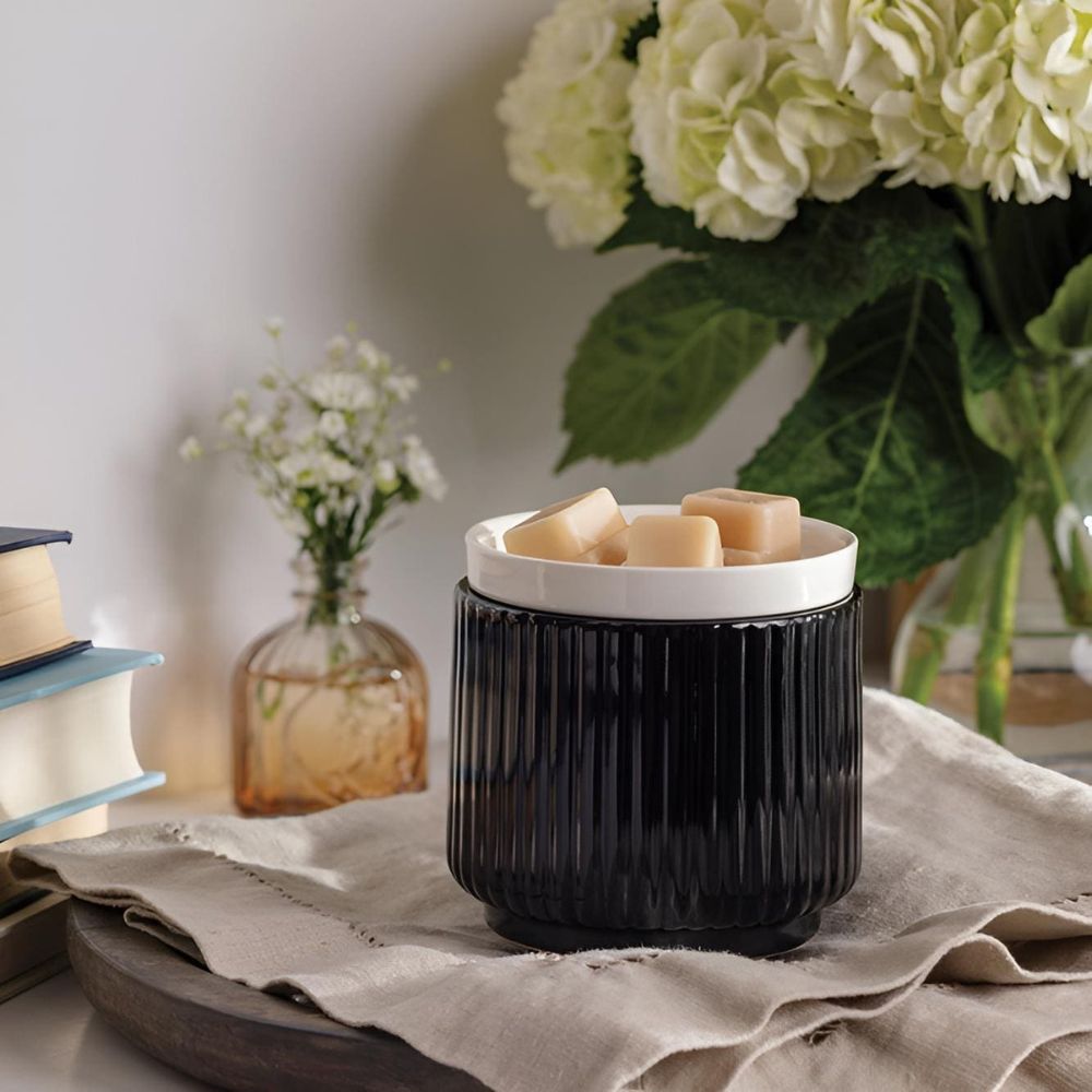La Lampe à parfum avec plaque chauffante noir/blanc vue sur un plateau en bois avec un linge en lin gris, chauffant des cire, devant un bouquet d'hortensias blancs