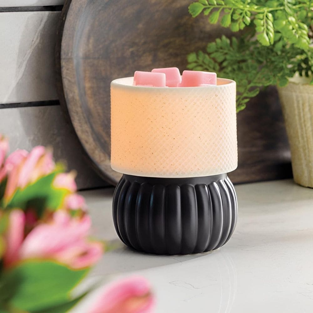 Gros plan sur la texture de la céramique et la finition noir mat de la Lampe chauffe-cire électrique Luxe posée sur un meuble.