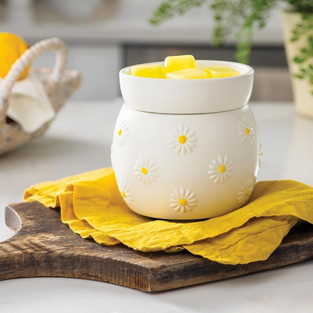 Lampe à parfum électrique Marguerite en céramique blanche avec fleurs en relief sur un linge jaune, chauffant des cubes de cire jaune.
